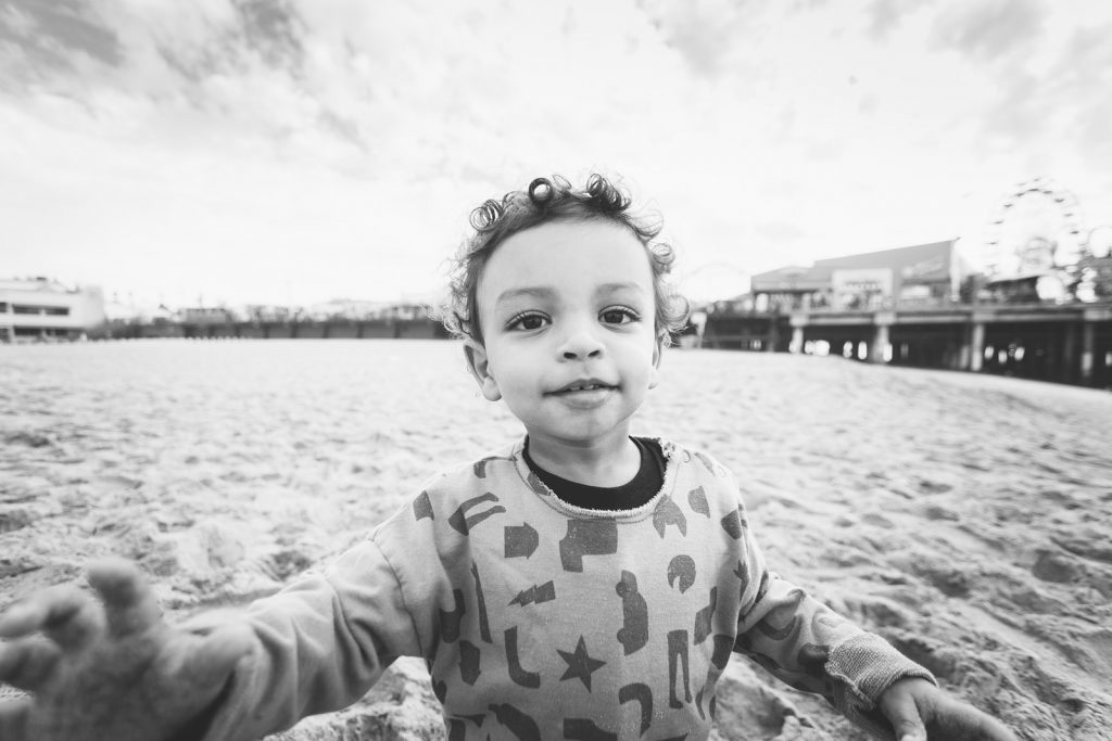 Black & white photo of a young boy on a southern California beach in Santa Monica. Family photography by Birchblaze.