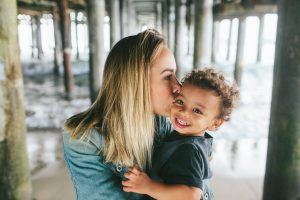 Color Photo of a mother kissing her young son under the Santa Monica Pier in southern California. Photo by Birch Blaze Studios.