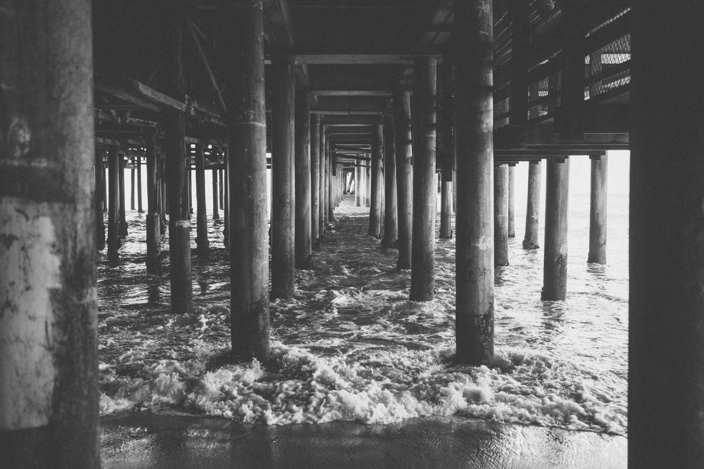 Black & white photograph of the Santa Monica Pier, taken beneath the Pier. Image by Birchblaze.