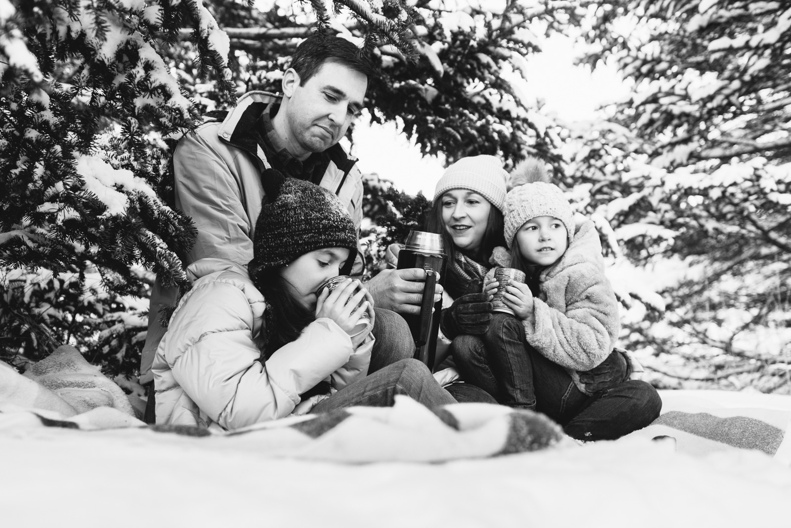 Family drinking hot chocolate under snowy pine trees. NH winter family lifestyle photography session by Birch Blaze Studios. https://birchblaze.com